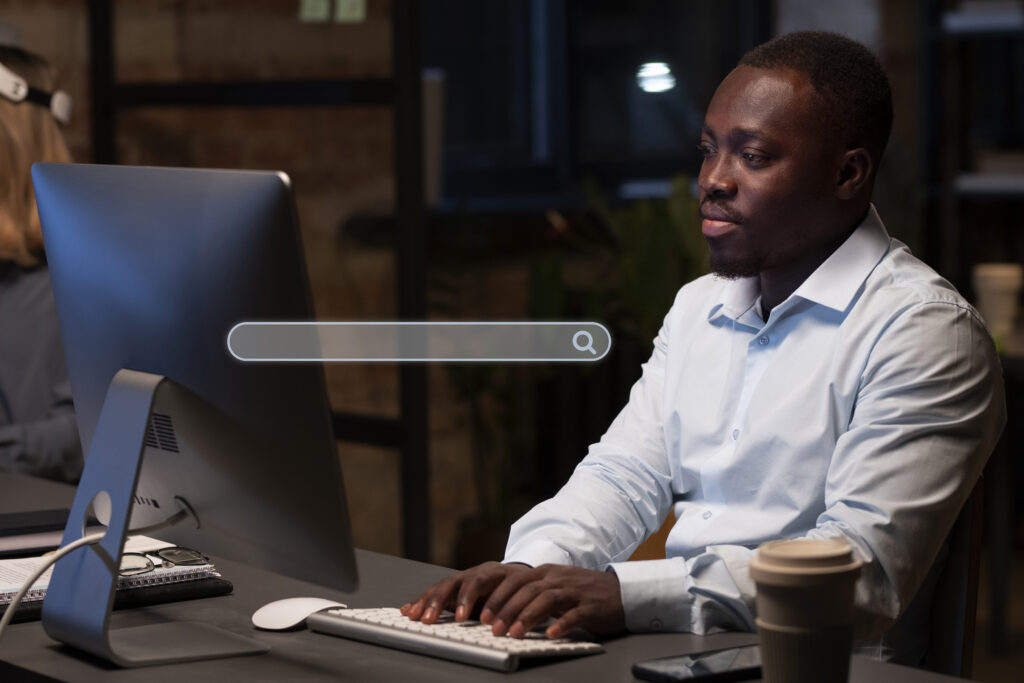 Focused man working on a desktop computer, using a search engine to research better paid ad strategies at night.