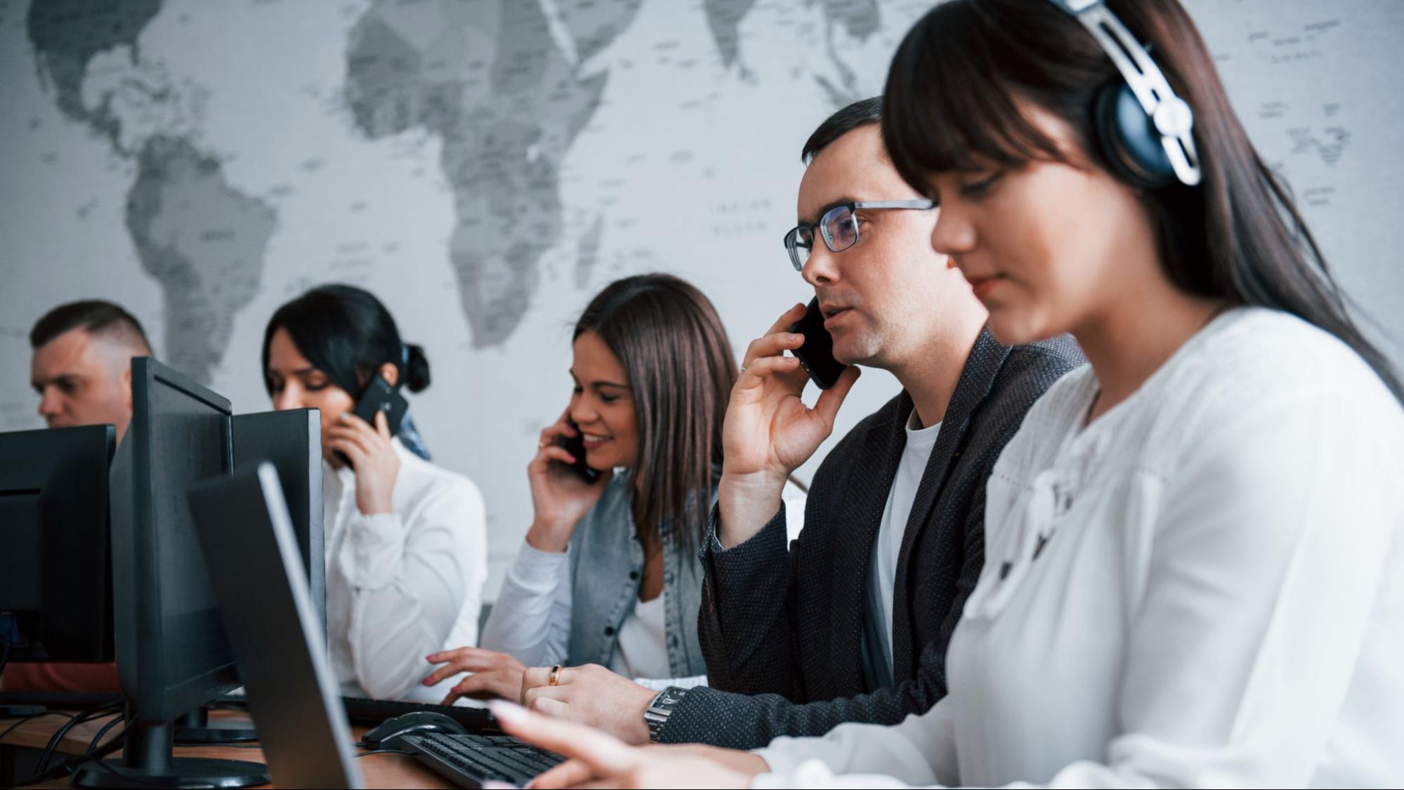 Diverse contact center team making client calls and managing real estate leads using computers in a high-volume work setting.