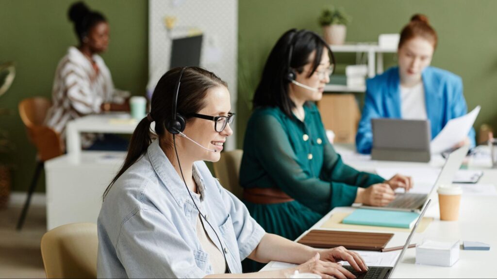 Team of real estate contact center agents managing client communications via laptops and headsets in a collaborative office space.